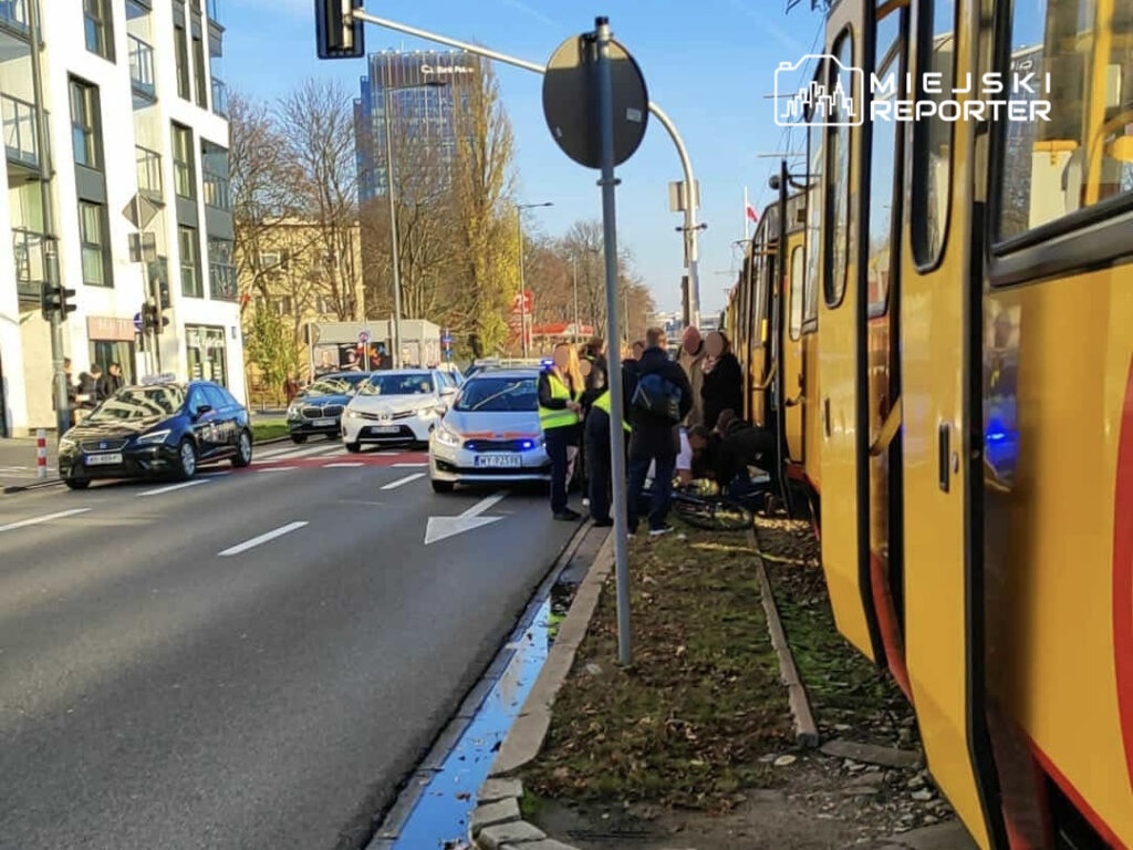 Na ulicy zatrzymują się samochody, a obok tramwaju zbiera się grupa ludzi oraz policja.