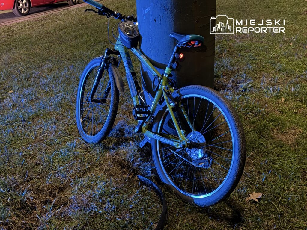 Zielony rower górski oparty o betonowy słup w oświetlonym nocą otoczeniu trawnika.