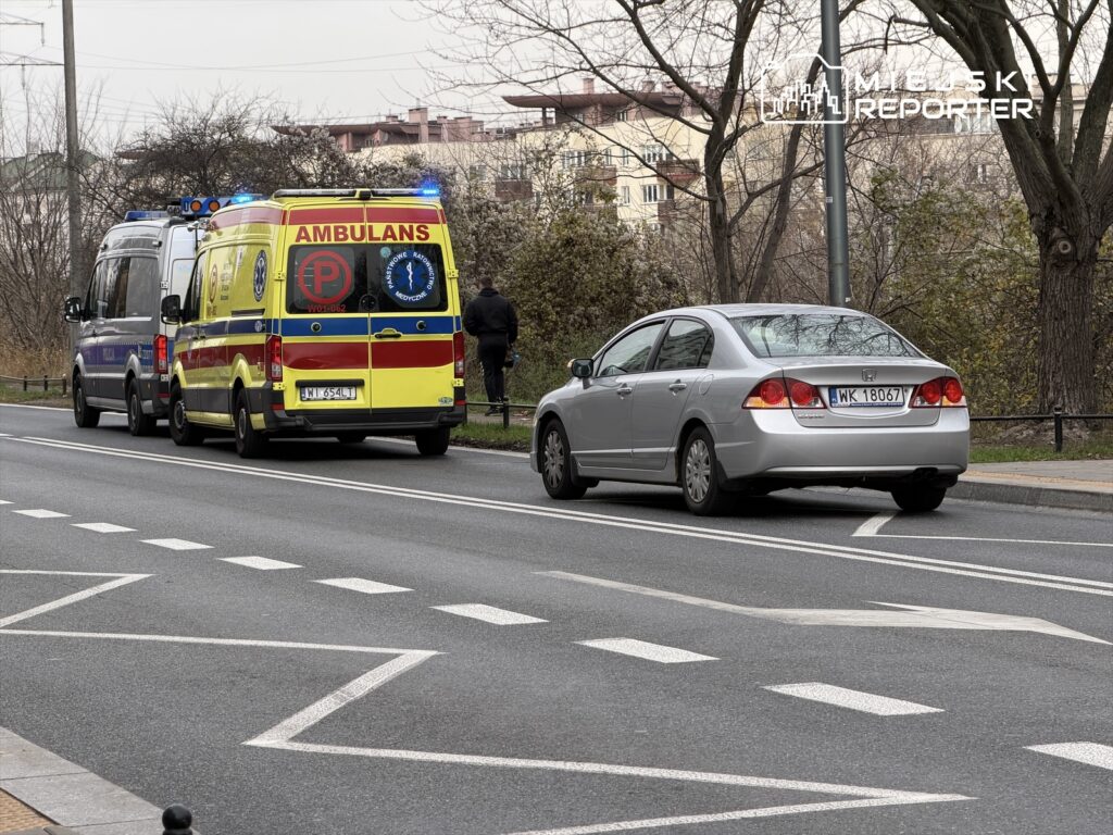Karetka pogotowia i policyjny van zatrzymane na drodze, obok stoi mężczyzna w mundurze.