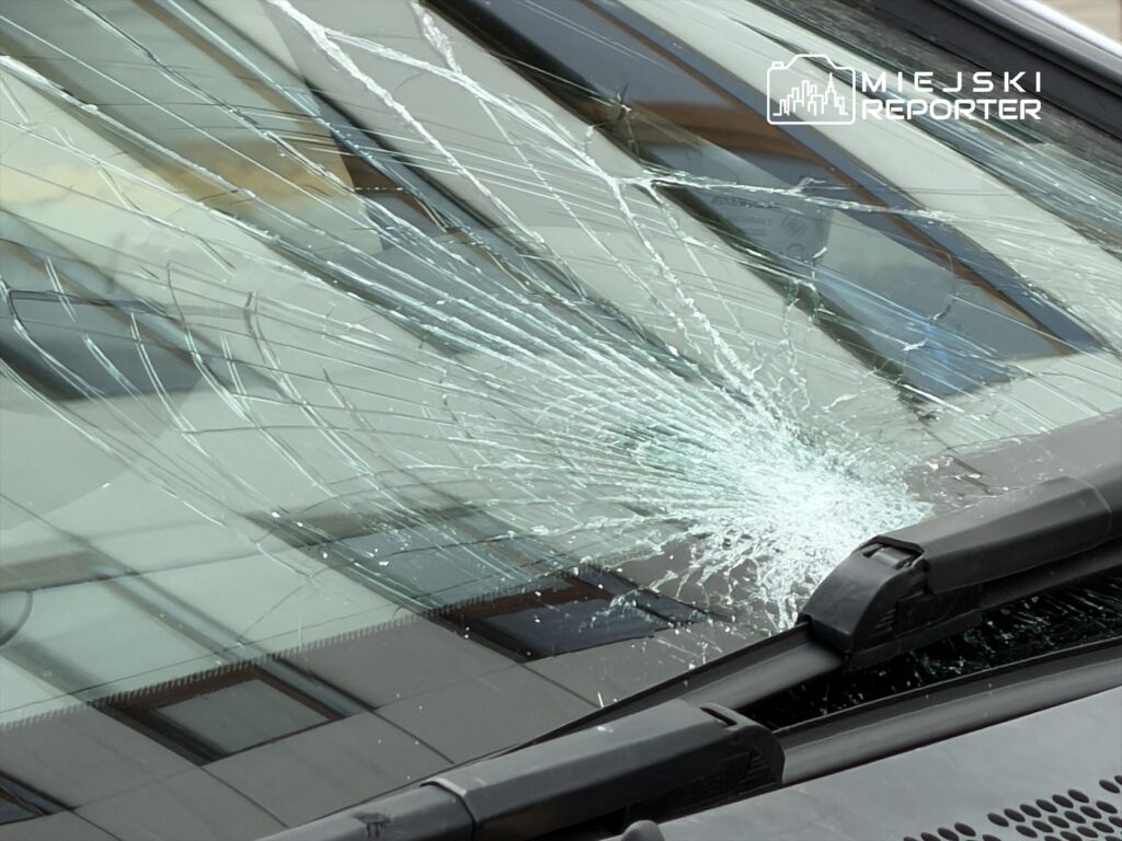 Szyba przednia samochodu z rozległym pęknięciem, w tle odbicia budynków.