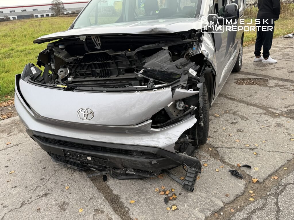 Uszkodzony samochód osobowy marki Toyota z uszkodzoną przednią częścią stoi na poboczu drogi, obok stoi mężczyzna.