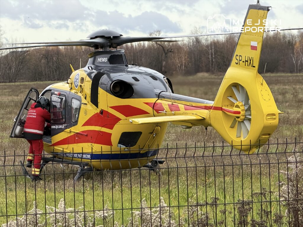 Ratownik w czerwonym uniformie wchodzi do śmigłowca medycznego na otwartej przestrzeni w pobliżu lasu.