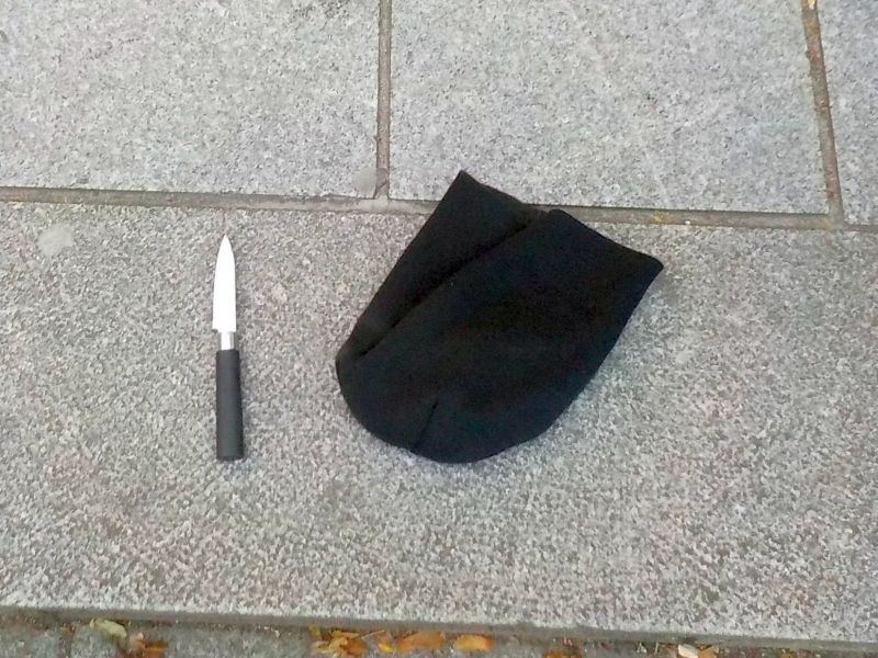 Nóż kuchenny i czarna skarpetka leżące na szarej kostce brukowej.