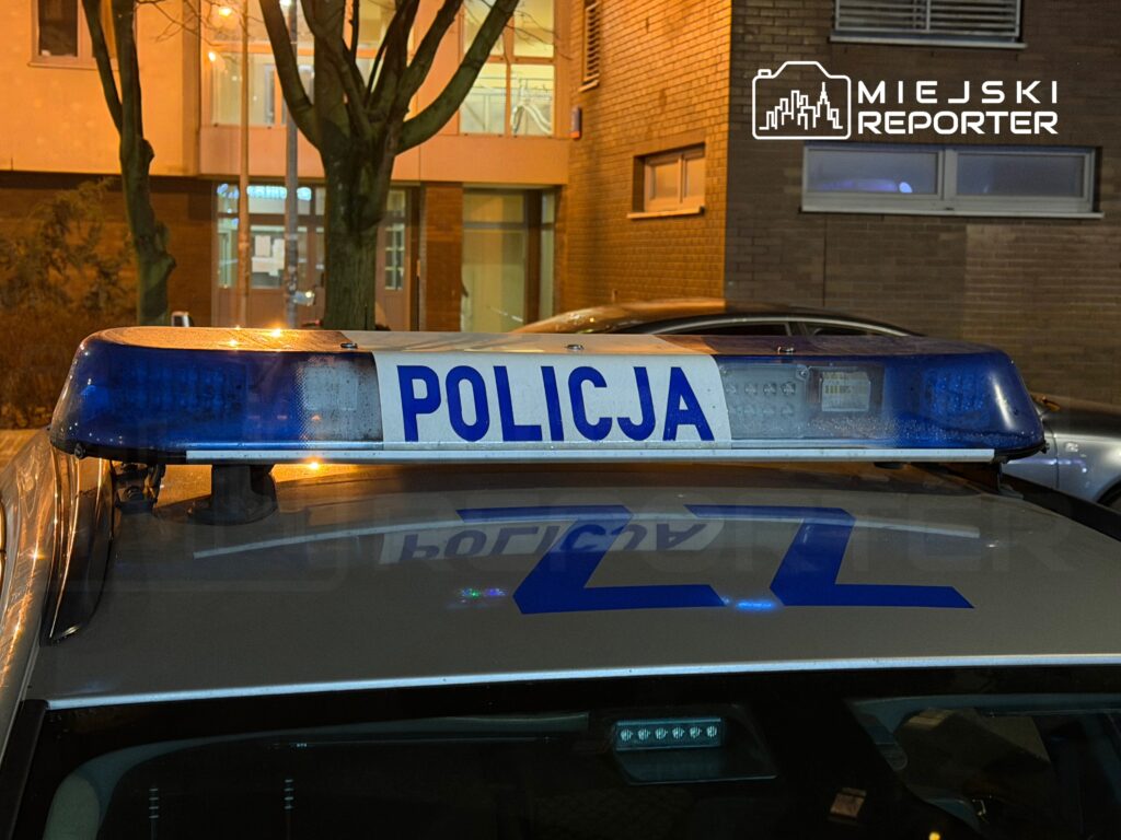 Niebiesko-biała lampka policyjna zamontowana na dachu radiowozu, stojącego w miejskim otoczeniu nocą.