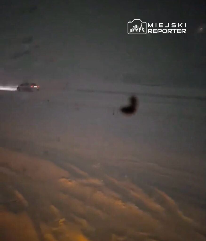 Samochód porusza się po ośnieżonej drodze w trudnych warunkach pogodowych, z widocznością ograniczoną przez śnieg.