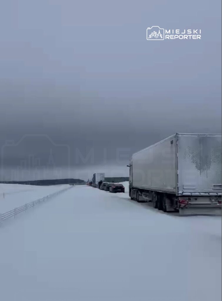Ruch ciężarówek i samochodów osobowych zatrzymany na zaśnieżonej drodze w zimowym krajobrazie.