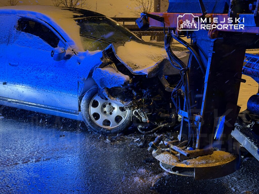 Zniszczony samochód osobowy z wgniecioną przednią częścią stoi na śliskiej drodze, obok maszyny do odśnieżania.