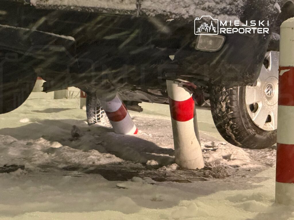 Samochód uniesiony na słupkach w śnieżnym otoczeniu, z widoczną oponą i podwoziem.