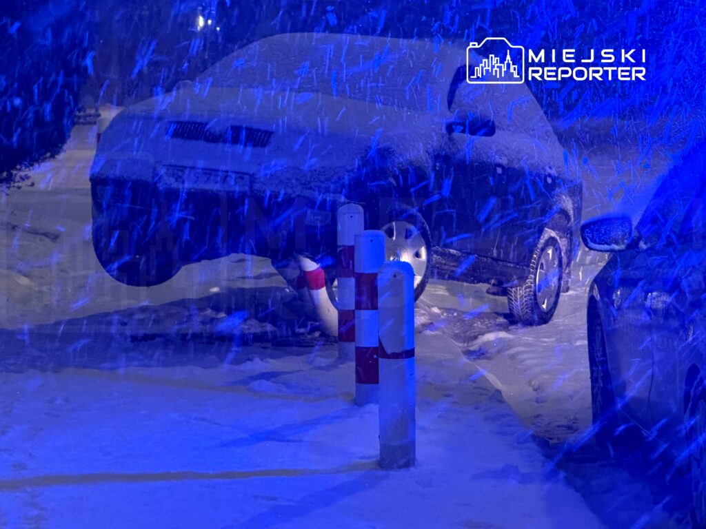 Samochód pokryty śniegiem stoi na ośnieżonej ulicy, a w tle widać padający śnieg.
