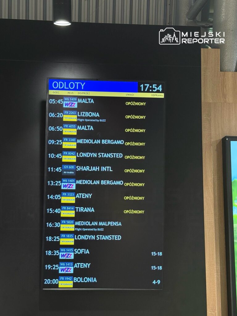 Tablica odlotów na lotnisku z informacjami o opóźnionych lotach do różnych miast, w tym Malty i Lizbony.
