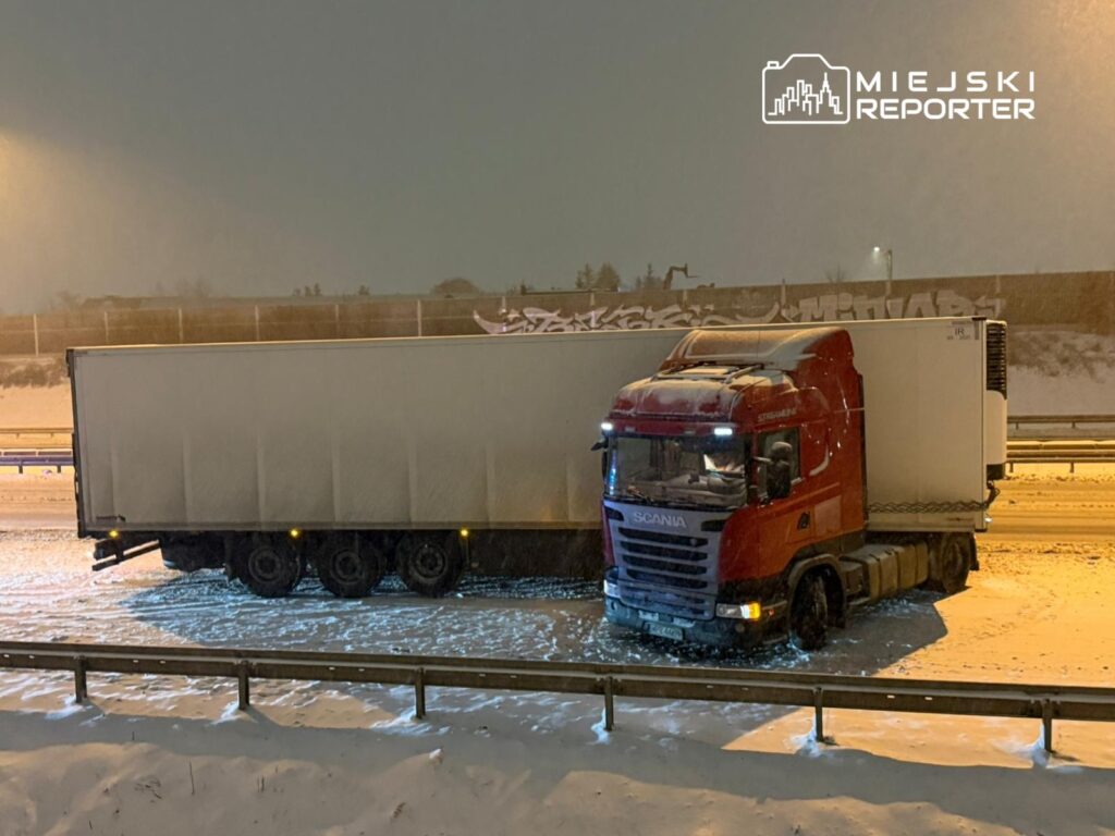 Czerwony ciągnik siodłowy z naczepą stoi na zaśnieżonej drodze, otoczony przez białą pokrywę śniegu.