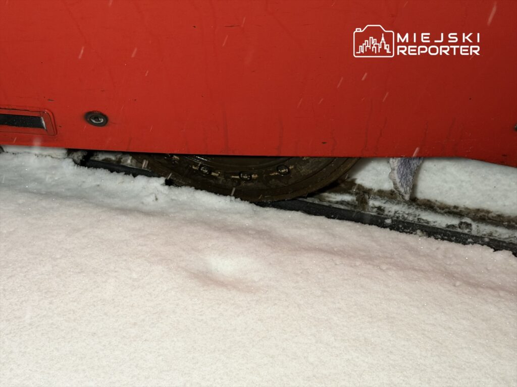 Czerwony pojazd z gąsienicami porusza się po pokrytej śniegiem nawierzchni.