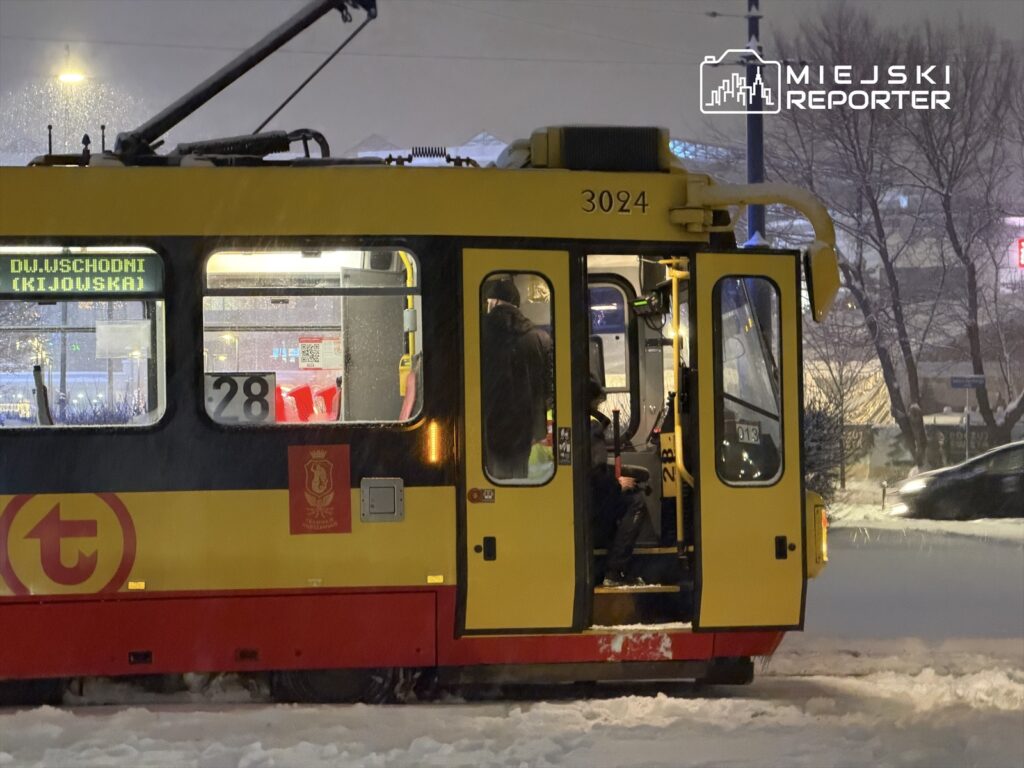 Żółty tramwaj z oznaczeniem "DW.JSCHODNI (KIJOWSKA)" zatrzymany w zaśnieżonym otoczeniu, z kierowcą w kabinie.