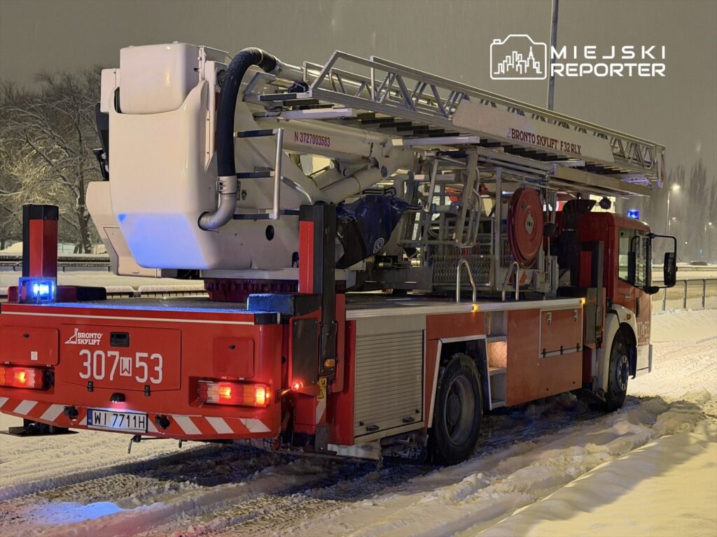 Czerwony wóz strażacki z podnośnikiem umieszczonym z tyłu stoi na zaśnieżonej drodze nocą.