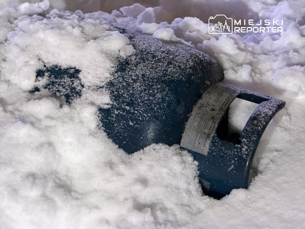 Niebieski zbiornik gazowy częściowo zakopany w śniegu, otoczony białą pokrywą śnieżną.