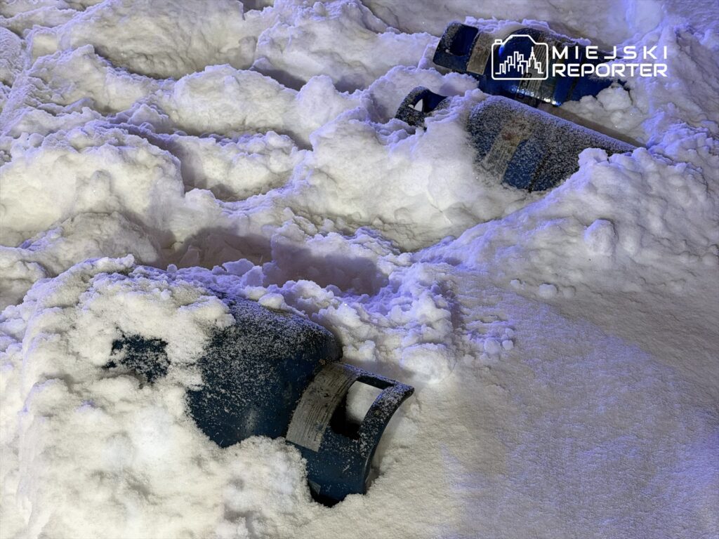 Dwa niebieskie zbiorniki gazowe częściowo zakopane w świeżym śniegu.