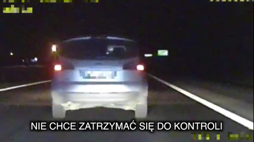 Samochód osobowy jedzie nocą po drodze, z napisem "NIE CHCE ZATRZYMAĆ SIĘ DO KONTROLI" widocznym na ekranie.