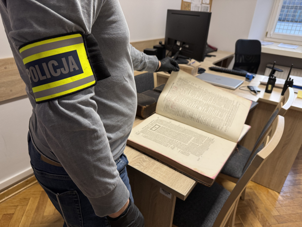 Policjant w szarym uniformie przegląda otwartą, starą księgę na biurku w biurze.