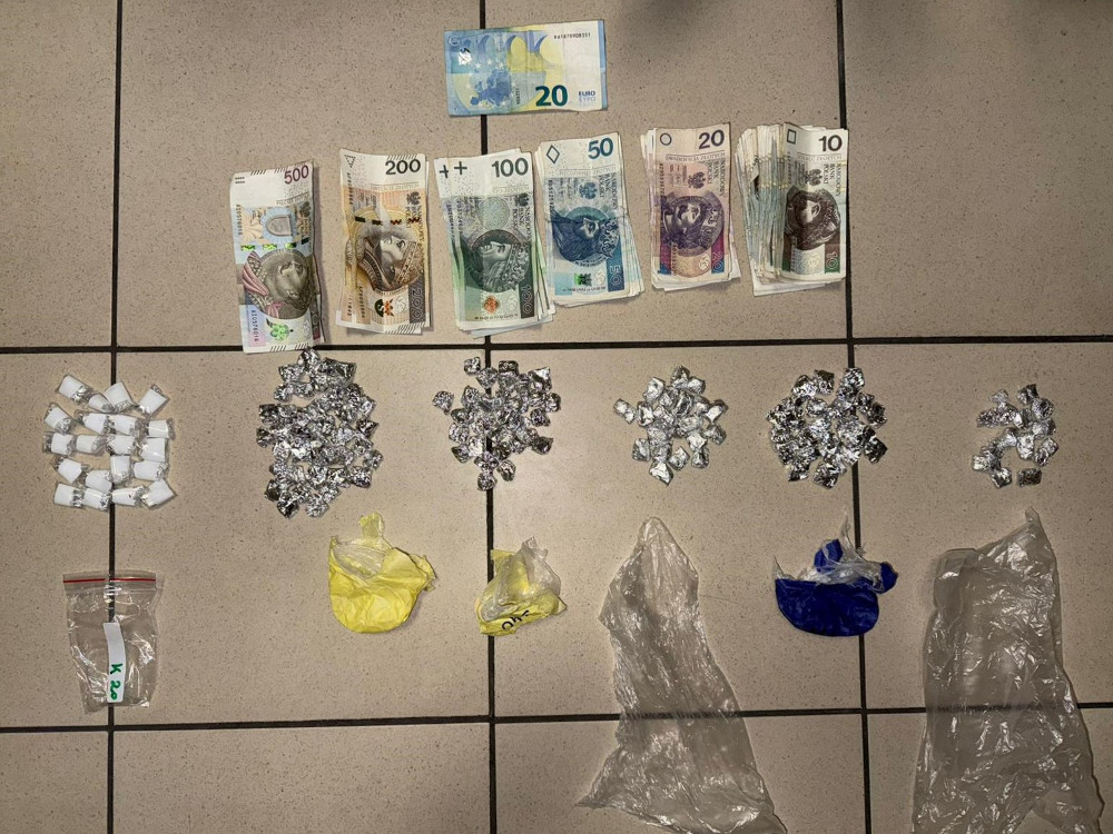 Na podłodze ułożone są banknoty w różnych nominałach oraz pakunki z substancjami, w tym białe woreczki i foliowe torebki.