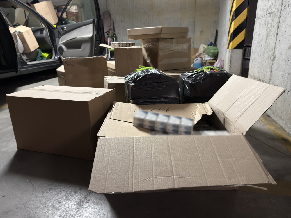Pojazd zaparkowany w garażu, obok otwartych kartonów i czarnych worków. W tle widoczne inne pudła.