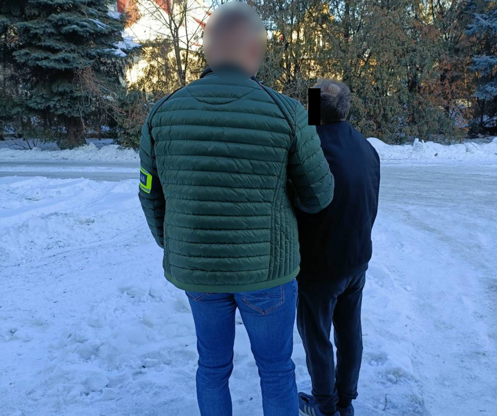 Funkcjonariusz w zielonej kurtce rozmawia z mężczyzną w czarnej odzieży na zaśnieżonej ulicy.