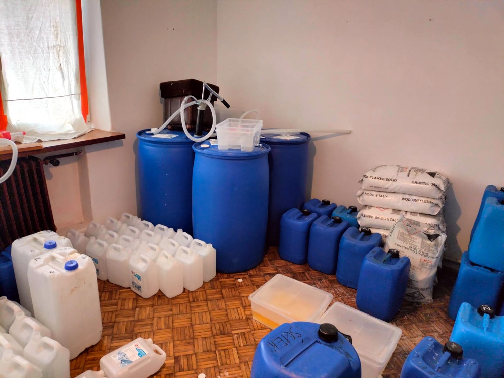 W pomieszczeniu znajdują się niebieskie beczki oraz plastikowe pojemniki, a także worki z substancjami chemicznymi.