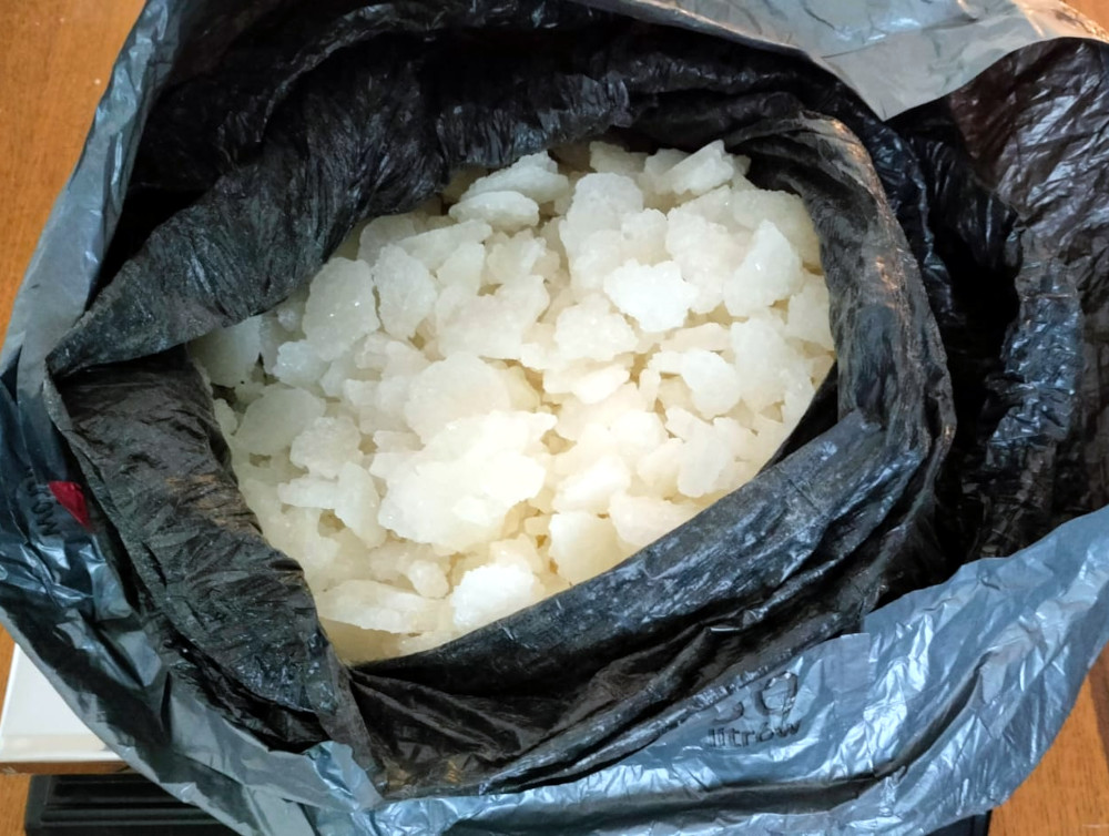 Czarny worek wypełniony białymi kryształkami, leżący na drewnianym blacie.