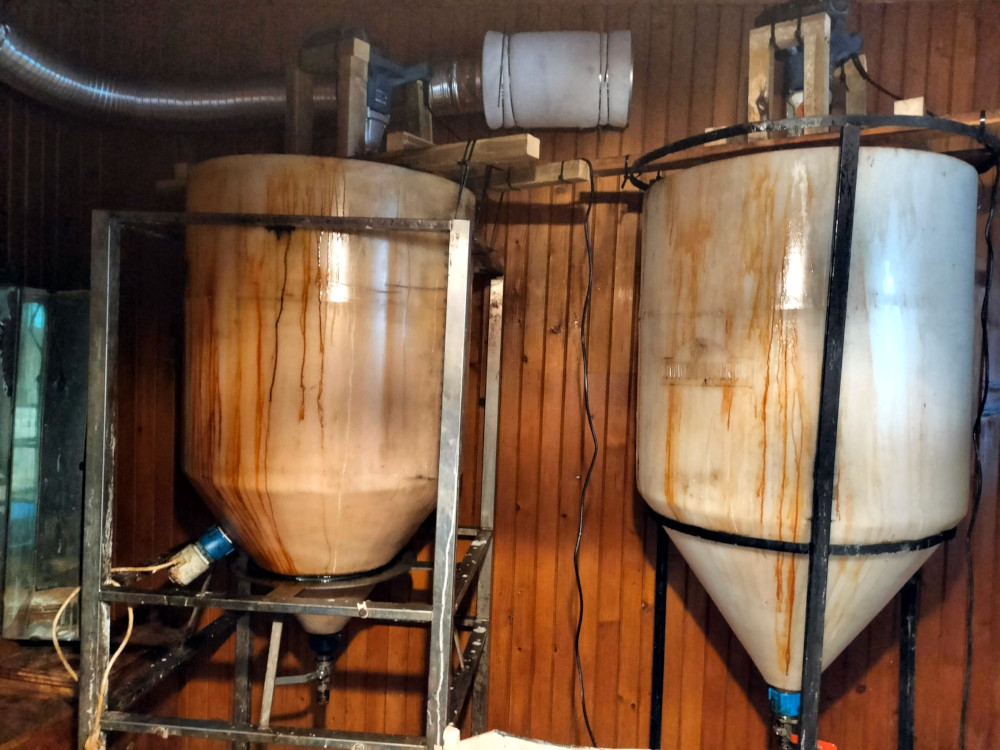 Dwa zbiorniki na ciecz umieszczone na stalowych stelażach w drewnianym pomieszczeniu, z widocznymi śladami płynów.