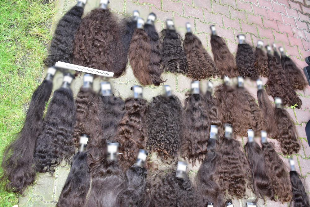 Zestaw naturalnych włosów w różnych odcieniach brązu, ułożony na kostce brukowej, z widocznymi klipsami.