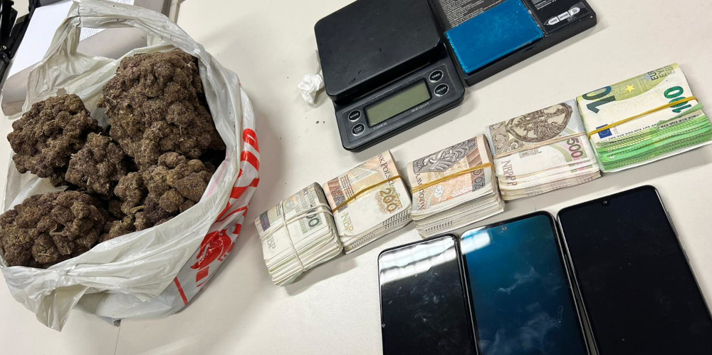 Torba z suszem roślinnym obok dwóch wag, stosu banknotów oraz trzech telefonów komórkowych na biurku.