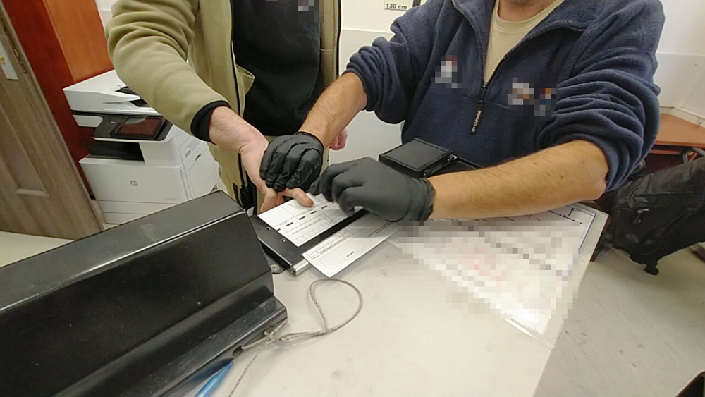 Dwaj mężczyźni w rękawiczkach pracują nad dokumentami na biurku w jasnym pomieszczeniu.