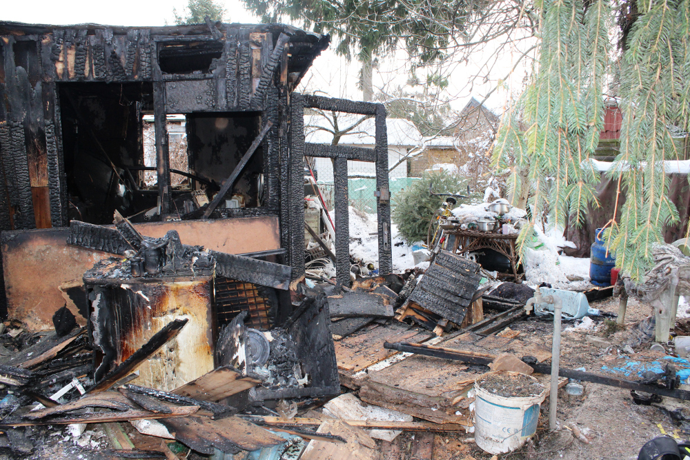 Zniszczony przez ogień budynek z czarnymi ścianami i zniszczonym wnętrzem, otoczony zamarzniętą ziemią i resztkami mebli.