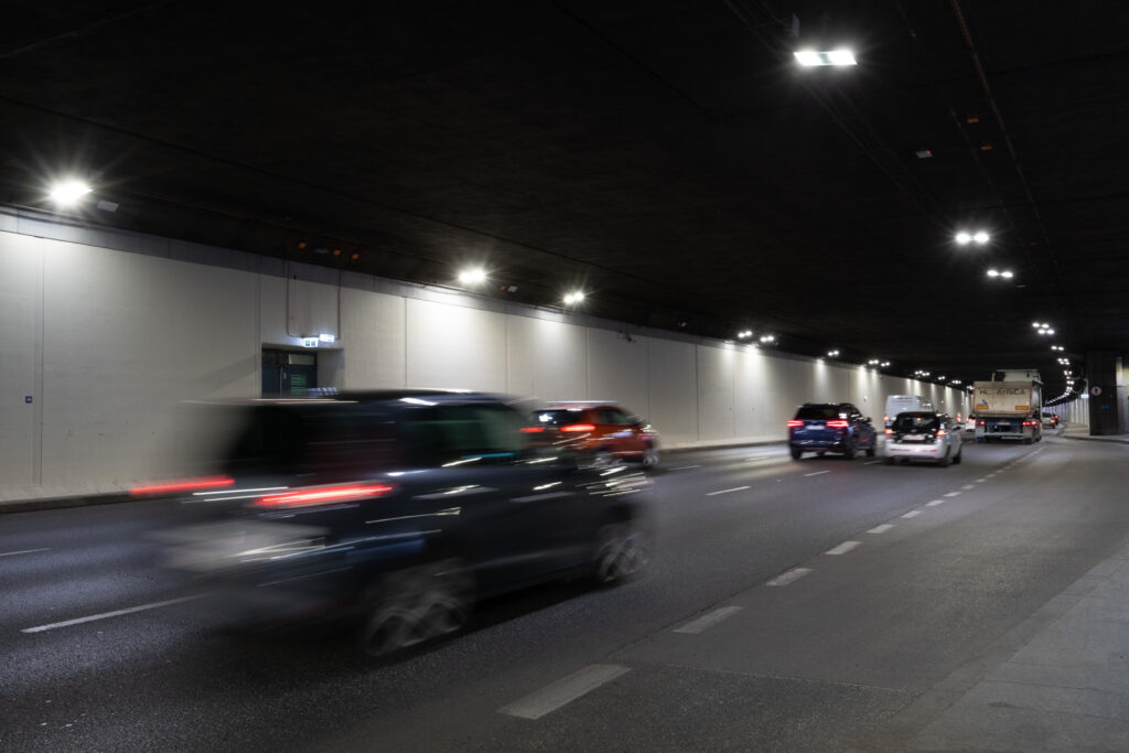 Samochody poruszające się z dużą prędkością w oświetlonym tunelu drogowym.