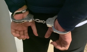 Mężczyzna w kajdankach stoi z rękami z tyłu, na tle jasnej ściany.