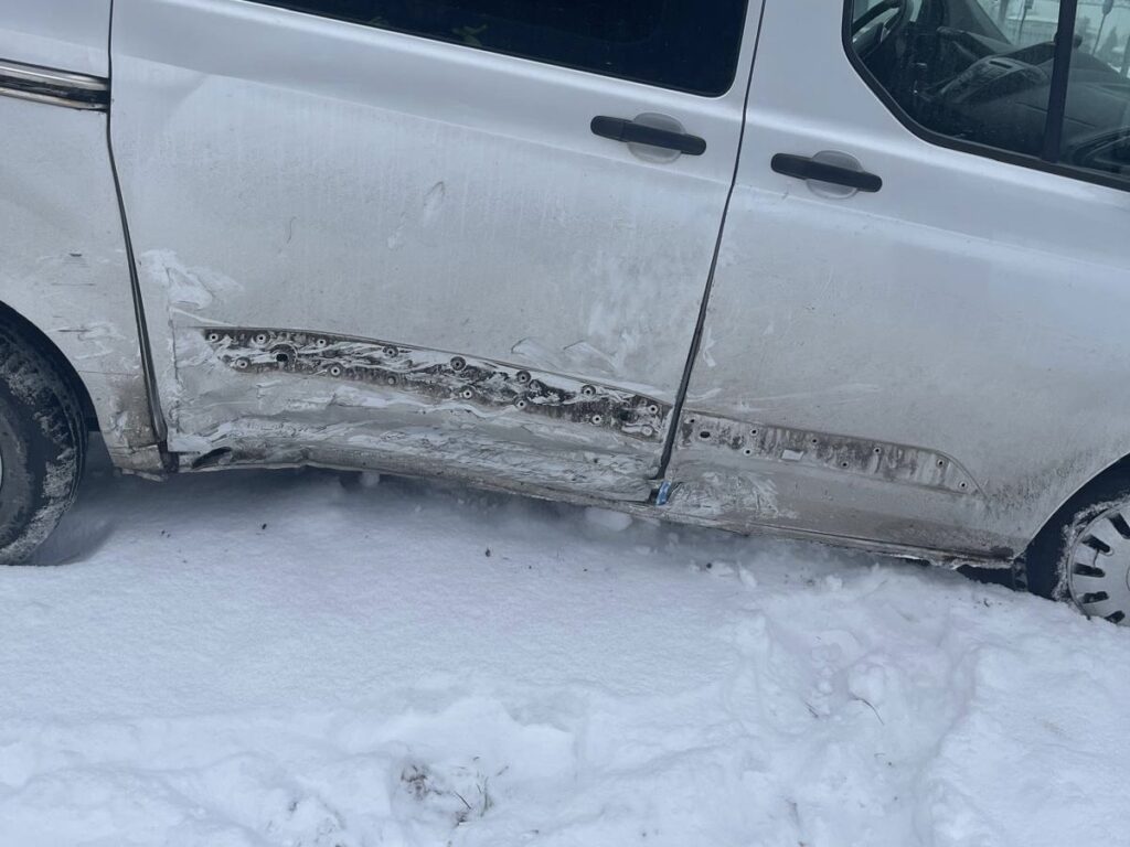 Uszkodzony biały samochód zaparkowany na zaśnieżonym terenie, z widocznymi zarysowaniami na drzwiach.