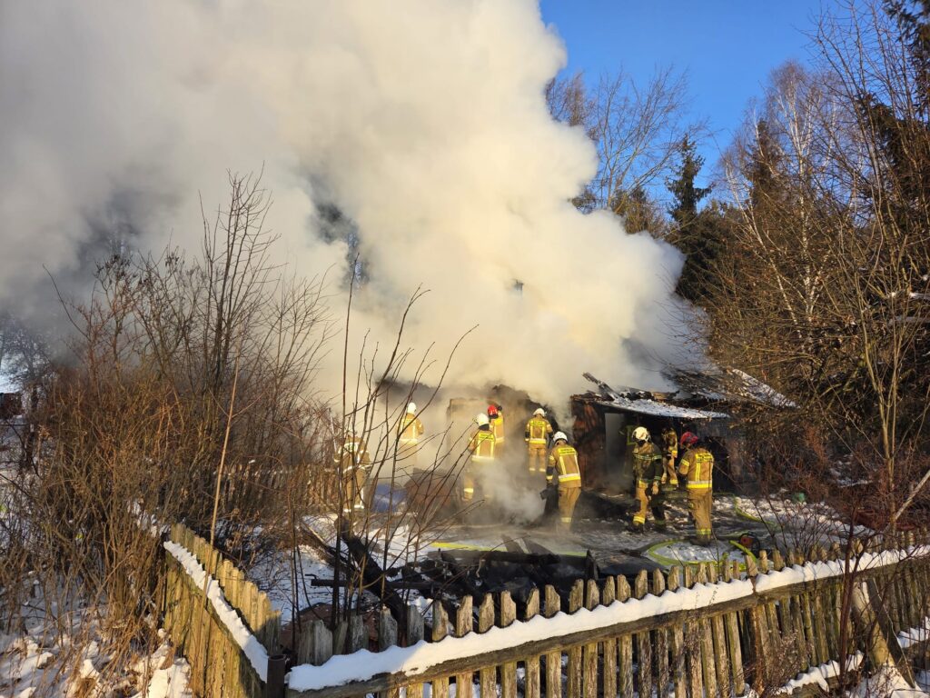 Strażacy gaszą pożar w zniszczonym budynku, otoczonym dymem i zimowym krajobrazem.