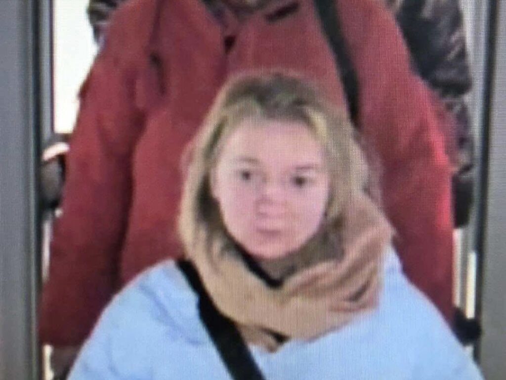 Młoda kobieta w jasnej kurtce z szalem, idąca w kierunku wyjścia, za nią osoba w czerwonej kurtce.