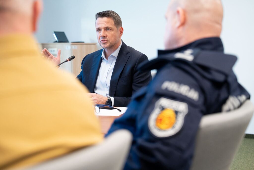 Mężczyzna w garniturze przemawia do grupy słuchaczy w sali konferencyjnej, z widocznym mikrofonem.