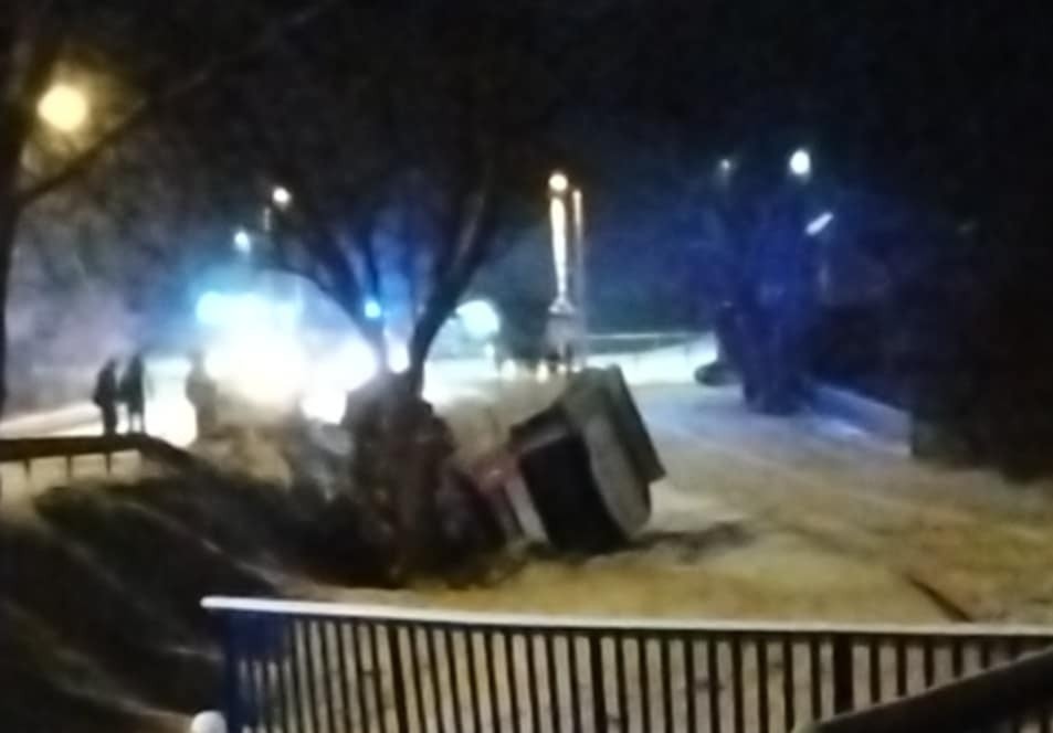 Pojazd przewrócony na bok na zaśnieżonej drodze, w tle widać radiowozy i grupę ludzi.
