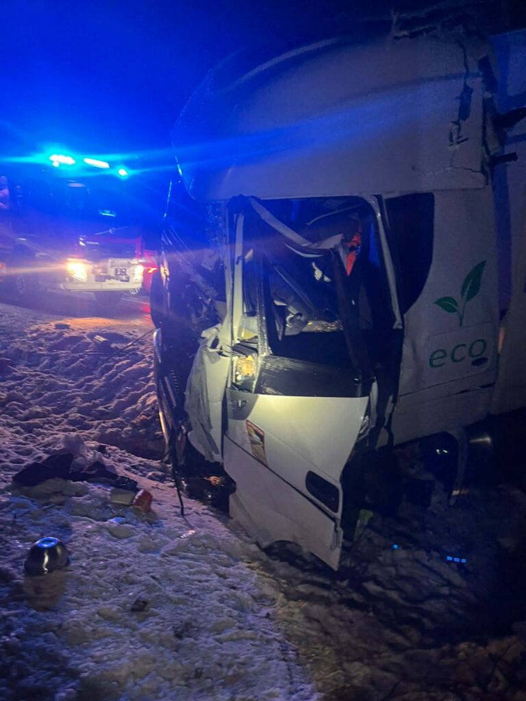 Cysterna leżąca na boku w zaśnieżonym terenie, obok widoczne niebieskie światła radiowozu.