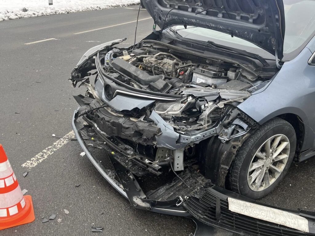 Uszkodzony samochód osobowy z rozbitą przednią częścią stoi na drodze, obok pomarańczowy słupek ostrzegawczy.