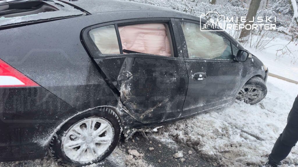 Czarny samochód osobowy z uszkodzeniem tylnych drzwi stoi na zaśnieżonej drodze. W tle widać drzewa pokryte śniegiem.