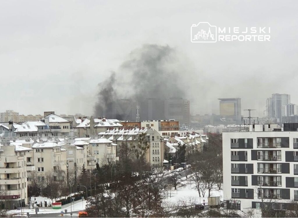 Gęsty, czarny dym unoszący się nad miastem w zimowy dzień, w otoczeniu pokrytych śniegiem budynków mieszkalnych.