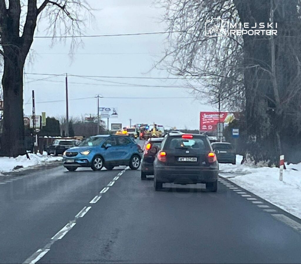 Niebieski samochód osobowy stoi na drodze, blokując ruch, w otoczeniu innych pojazdów w zimowej scenerii.
