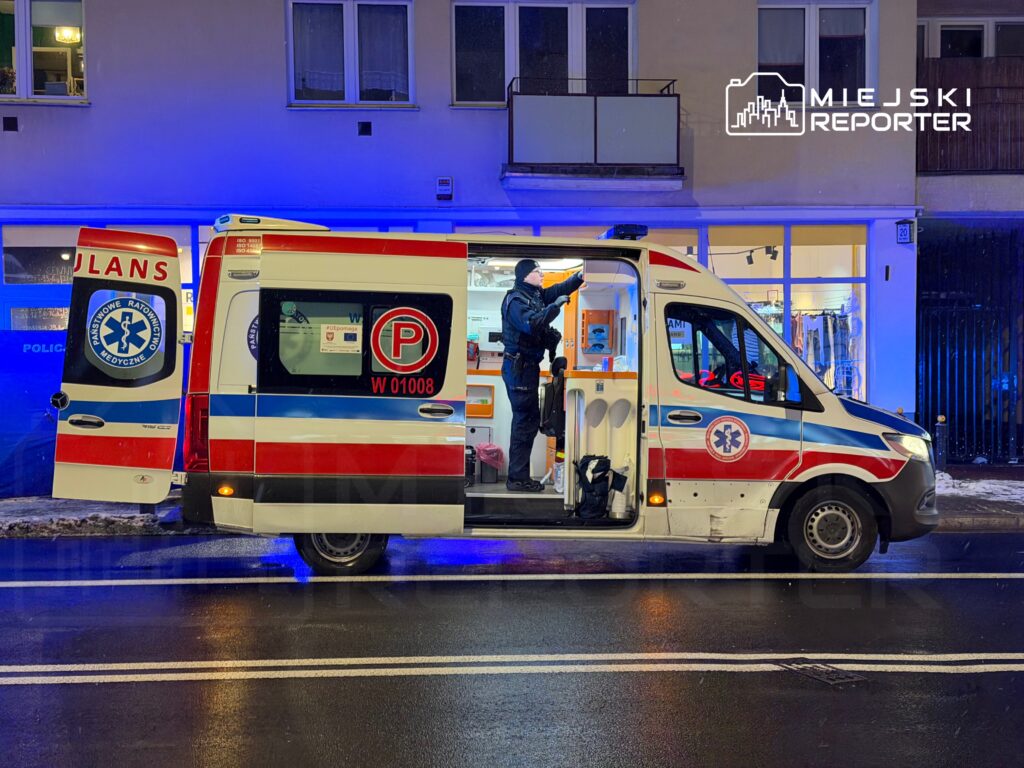 Karetka pogotowia z otwartymi drzwiami, ratownik medyczny przygotowujący sprzęt na ulicy w nocy.