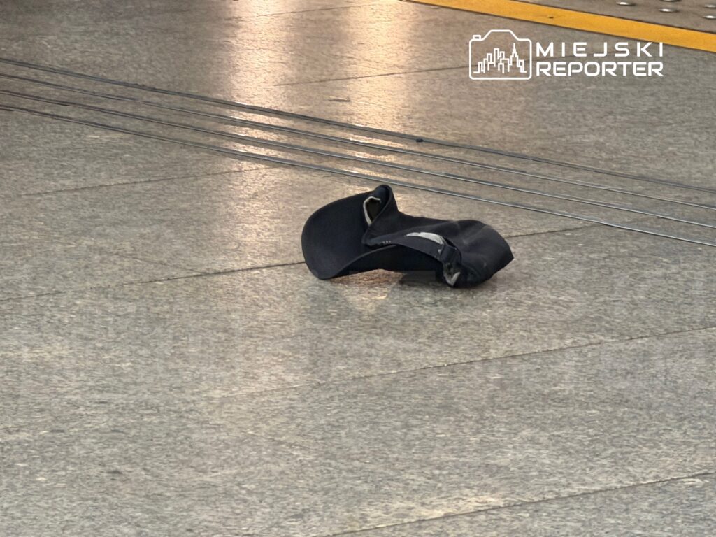 Czarna czapka leży na posadzce stacji tramwajowej obok torów.