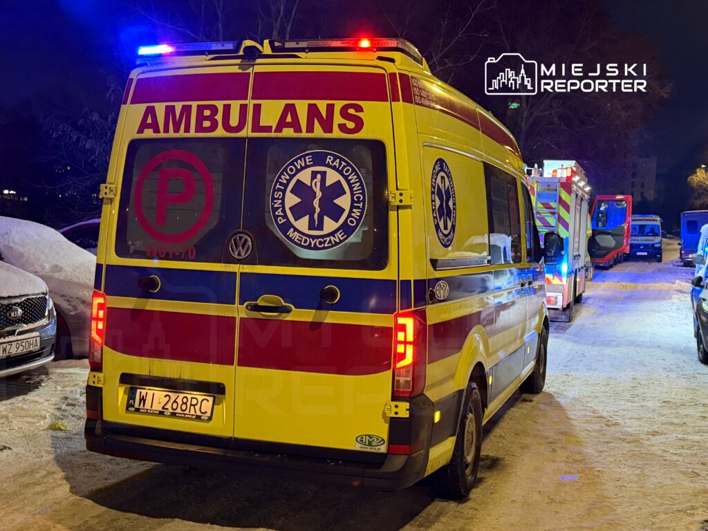 Karetka pogotowia z włączonymi sygnałami świetlnymi zaparkowana na zaśnieżonej ulicy nocą.