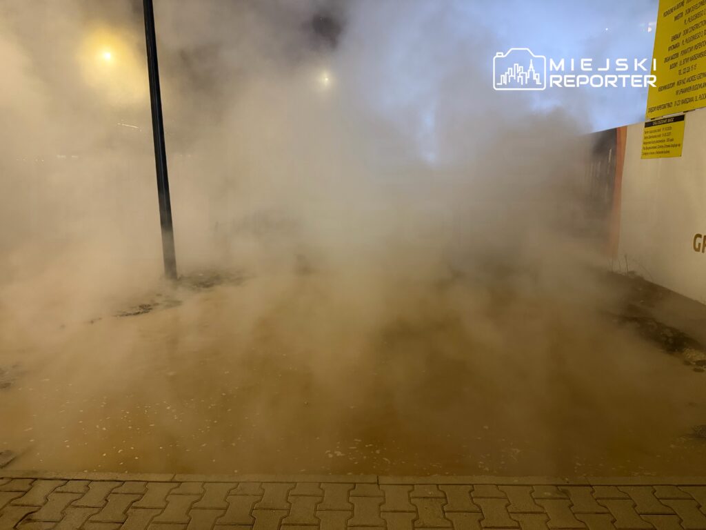 Gęsta mgła unosząca się nad chodnikiem, z latarnią oświetlającą otoczenie w tle.