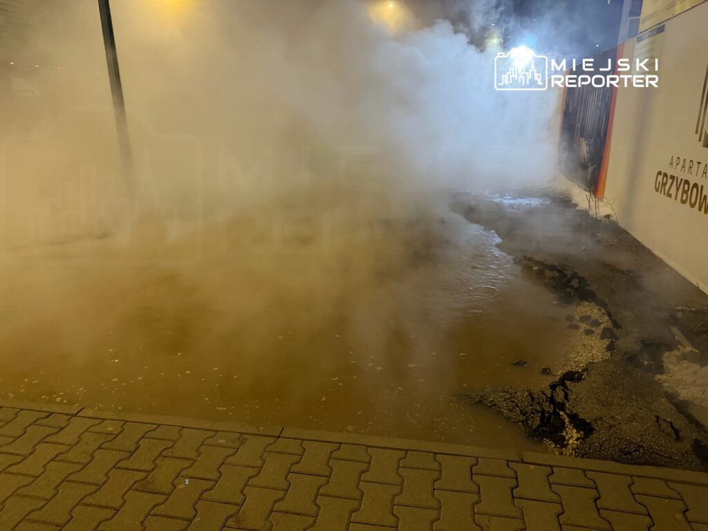 Gęsta mgła unosząca się nad zalaną nawierzchnią ulicy, obok uszkodzonej kostki brukowej.