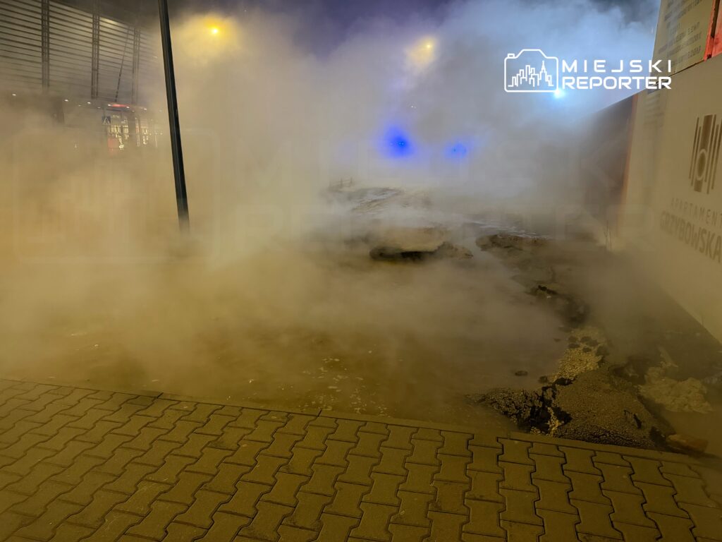 Gęsta mgła pary wodnej unosząca się nad uszkodzoną nawierzchnią chodnika w miejskim otoczeniu.